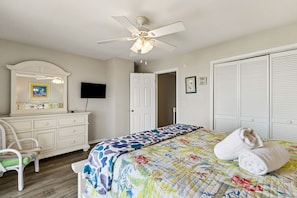 A bedroom with a bed, a dresser, a chair, a ceiling fan, a TV, and a closet.