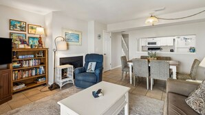 A living room with a fireplace, a bookshelf, a television, and a dining area with chairs and a table. - Relaxed Atmosphere in S Fletcher Duplex by RedAwning (Fernandina Beach)