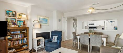 A living room with a fireplace, a bookshelf, a television, and a dining area with chairs and a table.