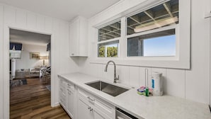 Una cocina con un lavamanos doble, armarios blancos y una ventana con vistas a zonas verdes.