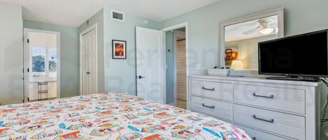 Un dormitorio con cama, cómoda, televisor y ventilador de techo.