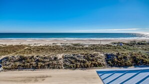 Vista de la playa con cielo despejado, arena y dunas.