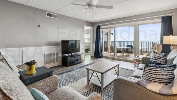 A spacious living room with a television, sofa, coffee table, and a view to the outside. - Amelia South 2 Bedroom Condo by RedAwning (Fernandina Beach)