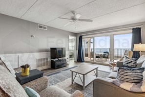 A spacious living room with a television, sofa, coffee table, and a view to the outside. - Amelia South 2 Bedroom Condo by RedAwning (Fernandina Beach)