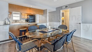 A modern kitchen with wooden cabinets, a glass dining table surrounded by wicker chairs, and a ceiling fan. - Amelia South 2 Bedroom Condo by RedAwning (Fernandina Beach)
