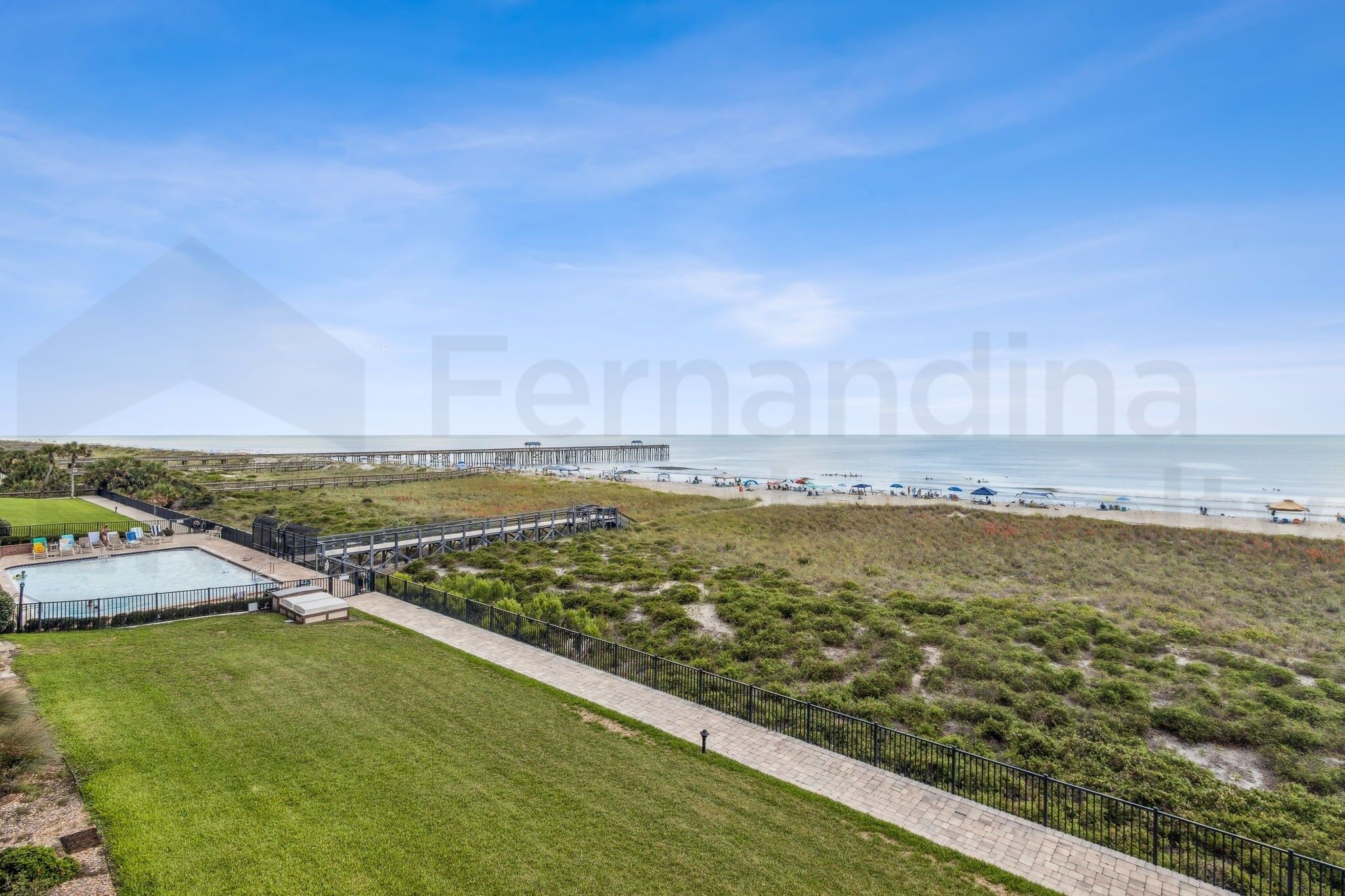A coastal view with a beach, a pier, and a swimming pool.