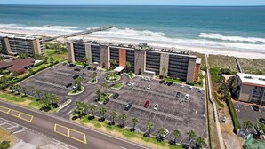 A parking lot with multiple cars, a beach, and a pier in the background. - Amelia South 2 Bedroom Condo by RedAwning (Fernandina Beach)
