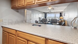 A kitchen with wooden cabinets, a granite countertop, and a dining area with a table and chairs. - Amelia South 2 Bedroom Condo by RedAwning (Fernandina Beach)