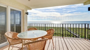 A balcony with wicker furniture and a glass table overlooking a beach and ocean. - Breathtaking Ocean View Amelia South Condo by RedAwning (Fernandina Beach)