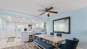 A modern kitchen with white cabinets, a central island, and a dining area with a table and chairs. - Striking Ocean View Condo with Private Walkway to the Beach by RedAwning (Fernandina Beach)
