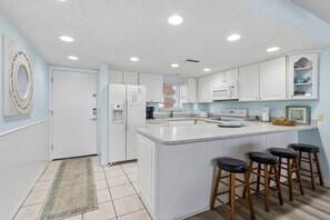 Una cocina con armarios blancos, una isla central con taburetes y un refrigerador y un microondas.