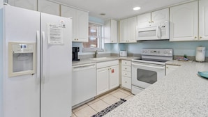 A kitchen with white cabinets, a refrigerator, a microwave, a stove, and a coffee maker. - Striking Ocean View Condo with Private Walkway to the Beach by RedAwning (Fernandina Beach)