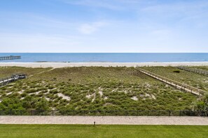 A beach with a wooden pier, a fenced area with vegetation, and a paved walkway. - Striking Ocean View Condo with Private Walkway to the Beach by RedAwning (Fernandina Beach)
