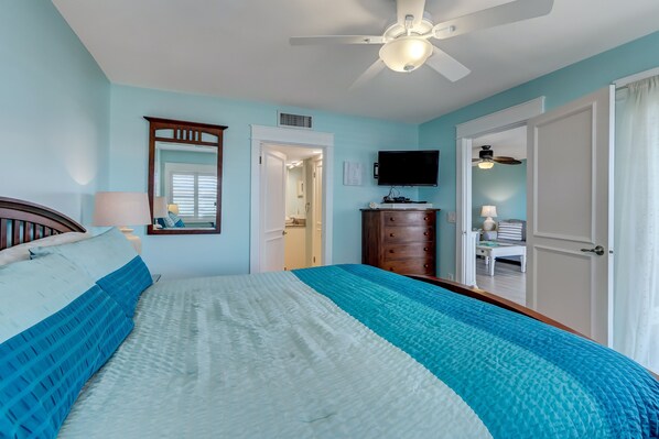 A bedroom with a bed, a ceiling fan, a TV, and a dresser.