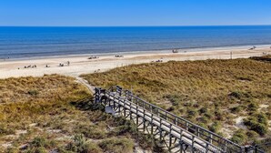 A beach with a wooden boardwalk leading to the shore, sandy beach, and clear blue sky. - Enhanced Unit with Awesome View of Atlantic from Private Balcony by RedAwning (Fernandina Beach)