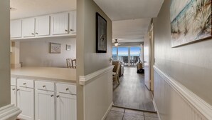 A hallway with white cabinetry, a framed picture, and a view to a dining area. - Enhanced Unit with Awesome View of Atlantic from Private Balcony by RedAwning (Fernandina Beach)