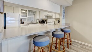 A modern kitchen with white cabinetry, a central island with stools, and a built-in oven. - Enhanced Unit with Awesome View of Atlantic from Private Balcony by RedAwning (Fernandina Beach)