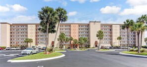 A multi-story hotel with a central courtyard, palm trees, and a parking lot with cars. - Enhanced Unit with Awesome View of Atlantic from Private Balcony by RedAwning (Fernandina Beach)