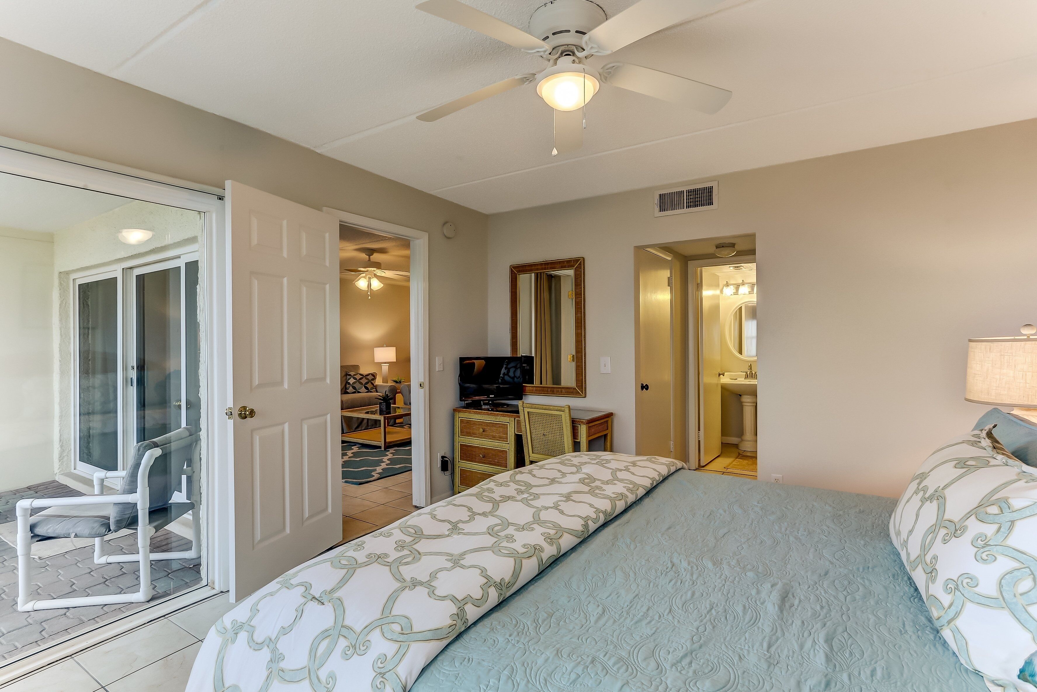A bedroom with a bed, a ceiling fan, a television, and a bathroom visible through an open door.