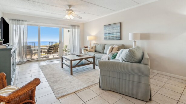 A spacious living room with a sofa, coffee table, and wicker chairs. A television is mounted on the wall, and there is a large window offering a view of the ocean. - Condo with Atlantic View from Private Patio, Short Walk to the Beach by RedAwning (Fernandina Beach)