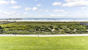 Un paisaje costero con una zona verde, un muelle de madera y una playa al fondo.