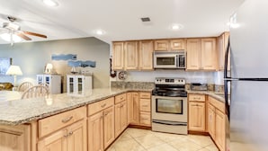 Cocina con armarios de madera, encimeras de granito, estufa, horno, microondas y refrigerador.