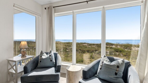 A balcony with a view of the beach, a sofa, a lamp, and a small table. - Renovated Seaside Condo with Gorgeous View of the Ocean by RedAwning (Fernandina Beach)