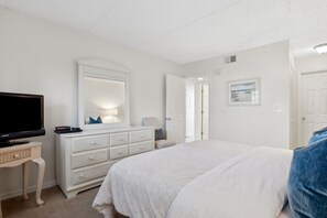 Une chambre à coucher comprenant un lit, une commode, un téléviseur et une porte donnant sur une autre pièce.