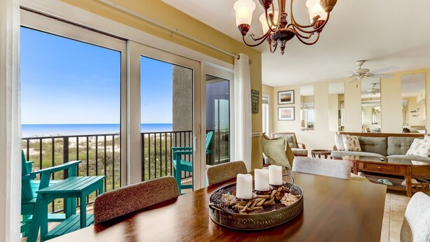 A spacious room with a large wooden dining table, teal chairs, and a view of the ocean through large sliding glass doors.