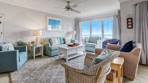 A living room with a ceiling fan, a white coffee table, two sofas, wicker chairs, a rug, and a view of the ocean. - Modern Condo with Amazing Ocean Front Views by RedAwning (Fernandina Beach)