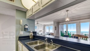 A kitchen with a double sink, a telephone, and a view of the balcony with chairs. - Modern Condo with Amazing Ocean Front Views by RedAwning (Fernandina Beach)
