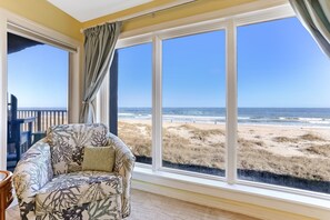 A room with a large window overlooking a beach, a cushioned chair, and a view of the ocean. - Seaboard Condo with Breathtaking Views of the Ocean by RedAwning (Fernandina Beach)