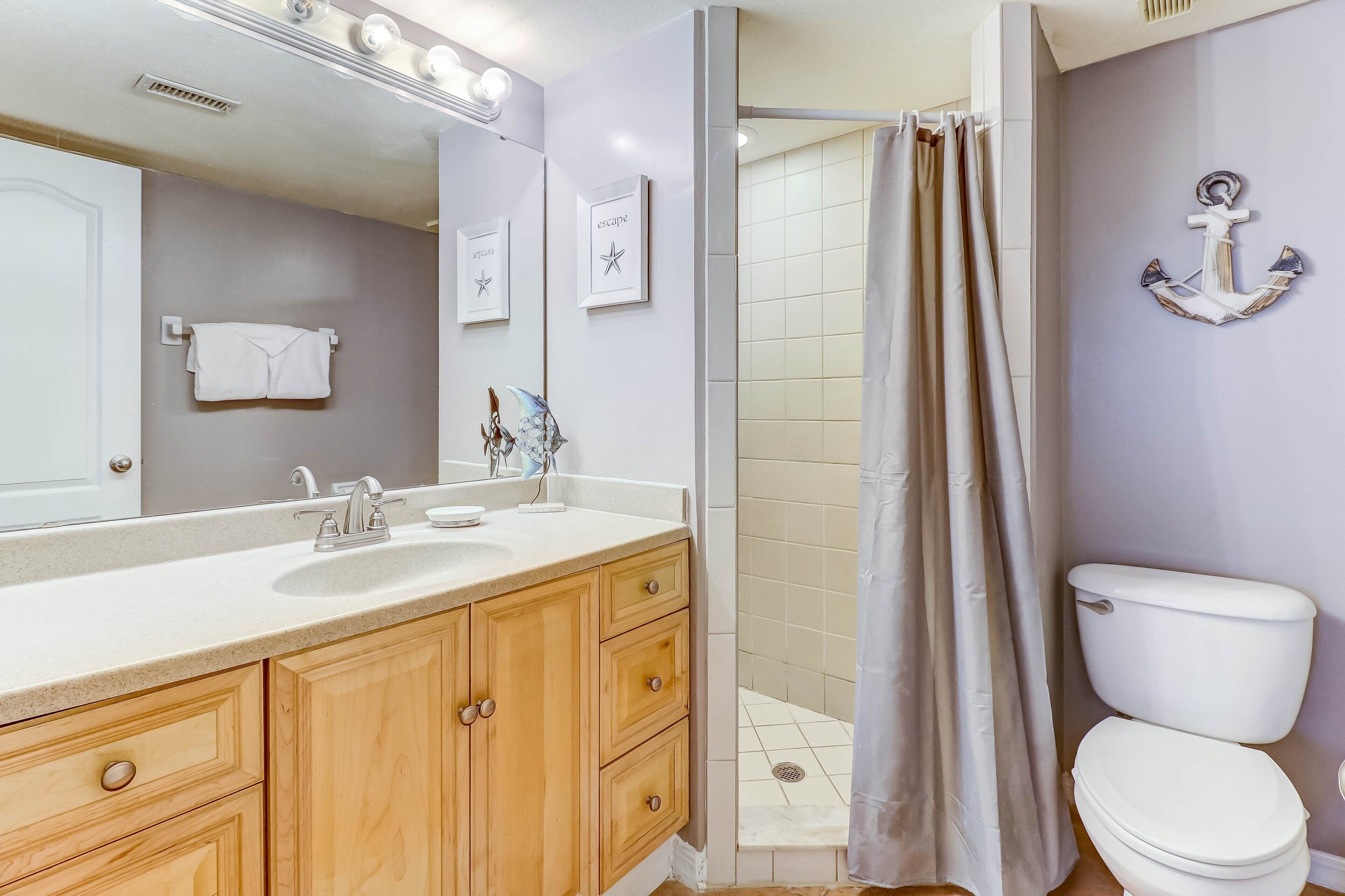Ein Badezimmer mit Waschbecken, Spiegel, Holzausbau, Toilette und Duschvorhang.