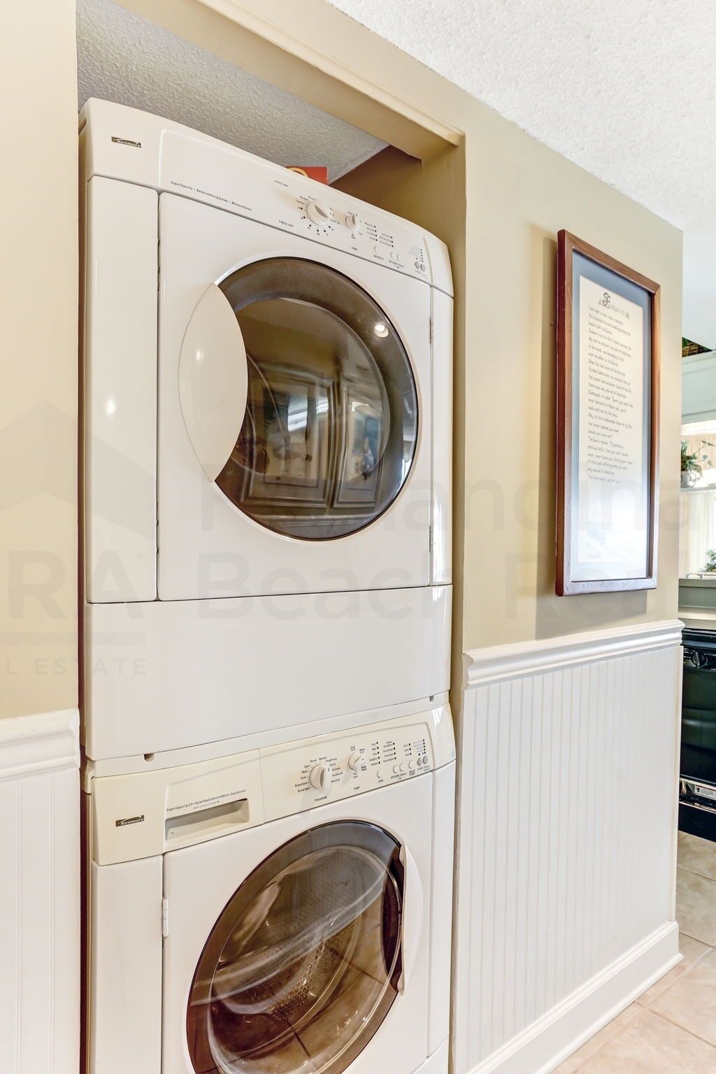 A stacked washer and dryer unit in a kitchen area with a framed certificate on the wall.