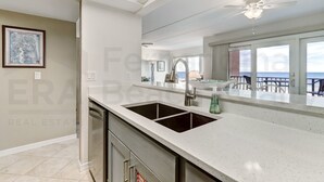 A kitchen with a double sink, stainless steel cabinets, and a large window overlooking the ocean. - Beautifully Decorated Condo with Magnificent View of Atlantic by RedAwning (Fernandina Beach)
