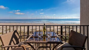 A balcony with a table and chairs overlooking a beach.