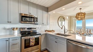 A modern kitchen with grey cabinets, stainless steel appliances, a large island with a sink, and a view of the ocean through large windows.