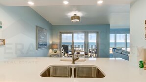 A modern kitchen with a stainless steel sink, a pendant light, and a view of the ocean through large windows.