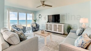 A living room with a large window, a ceiling fan, a television, and a cabinet.