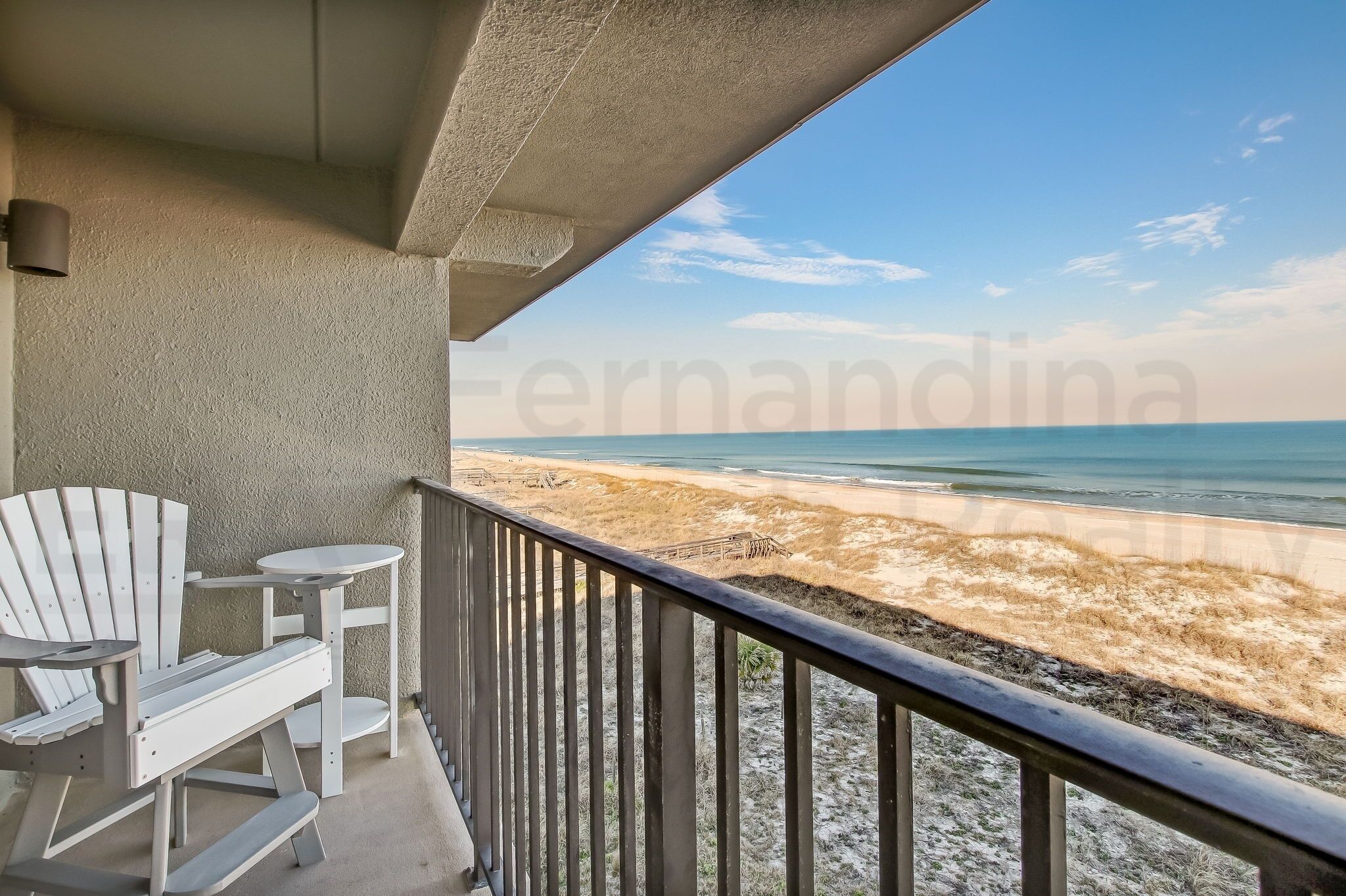 Un balcon avec vue sur la plage, agrémenté d’une chaise Adirondack blanche et d’une petite table ronde.