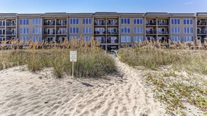 A multi-story building with balconies and a sandy path leading to it. - Coastal Condo with Ocean Viewing Pleasure by RedAwning (Fernandina Beach)