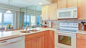A modern kitchen with wooden cabinets, a built-in microwave, a stove, and a dishwasher. - Coastal Condo with Ocean Viewing Pleasure by RedAwning (Fernandina Beach)