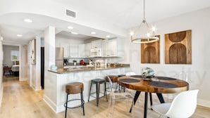 A modern kitchen with white cabinets, a central island with stools, and a dining area with a wooden table and chairs.