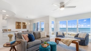 A modern living room with a grey sofa, teal ottomans, and a view of the ocean.