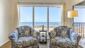 A room with two patterned armchairs facing a large window with a view of the beach. - Modest Condo with Splendid Sunrise Views by RedAwning (Fernandina Beach)