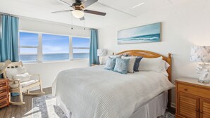 Ein Schlafzimmer mit einem großen Bett, einem Deckenventilator, Meerblick, einem Schaukelstuhl und einem Nachttisch aus Holz.