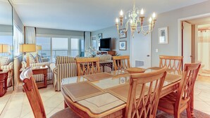 Un vaste espace dédié à la salle à manger, avec une grande table et des chaises en bois, un lustre et un téléviseur en arrière-plan.