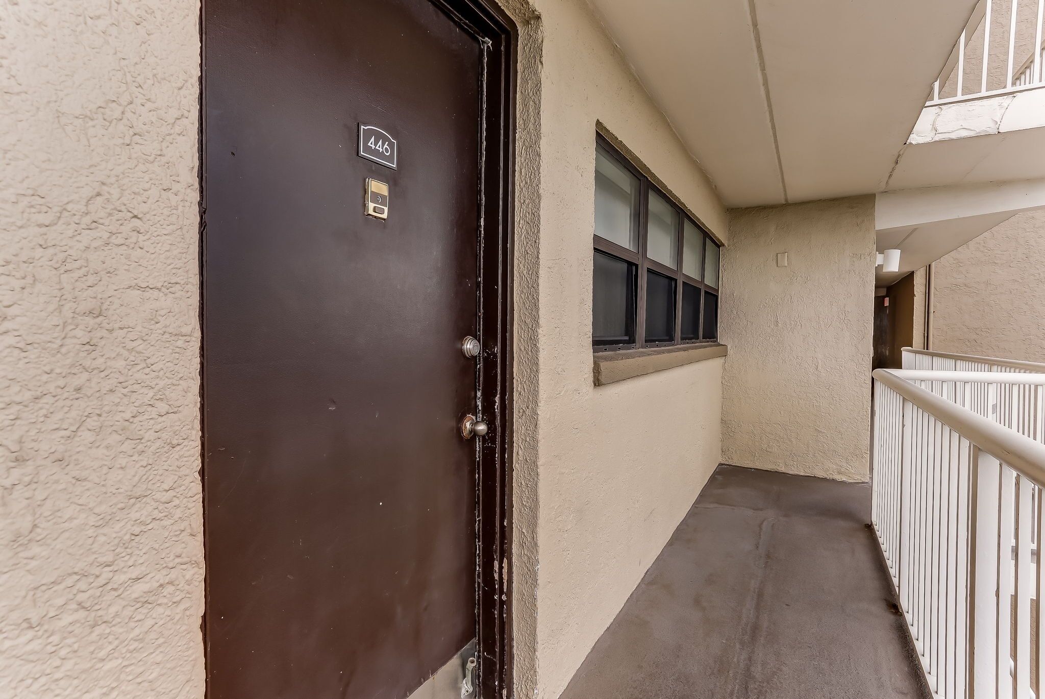 A narrow corridor with a dark brown door marked with the number 446, a window, and a white railing.