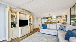 A spacious living room with a large sofa, a flat-screen TV, and a decorative cabinet. - Tastefully Decorated Condo with Scenic Beach Views by RedAwning (Fernandina Beach)