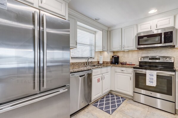 A modern kitchen with stainless steel appliances, white cabinetry, and a granite countertop.